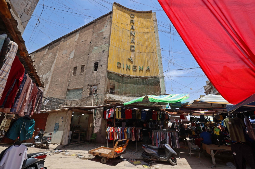 Street vendors gather outside the faded facade of the Granada Cinema, an early 1940s landmark, in the Bab al-Sharqi district of central Baghdad on May 26, 2026. (Photo by Ahmad Al-Rubaye/ AFP)