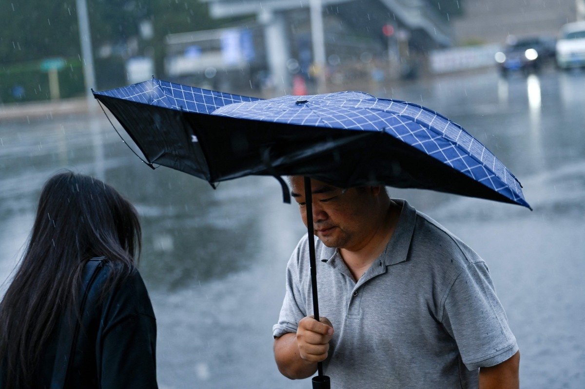 A man holding an umbrella walks along a road on a rainy day in Beijing on July 10, 2026. (Photo by WANG Zhao / AFP)