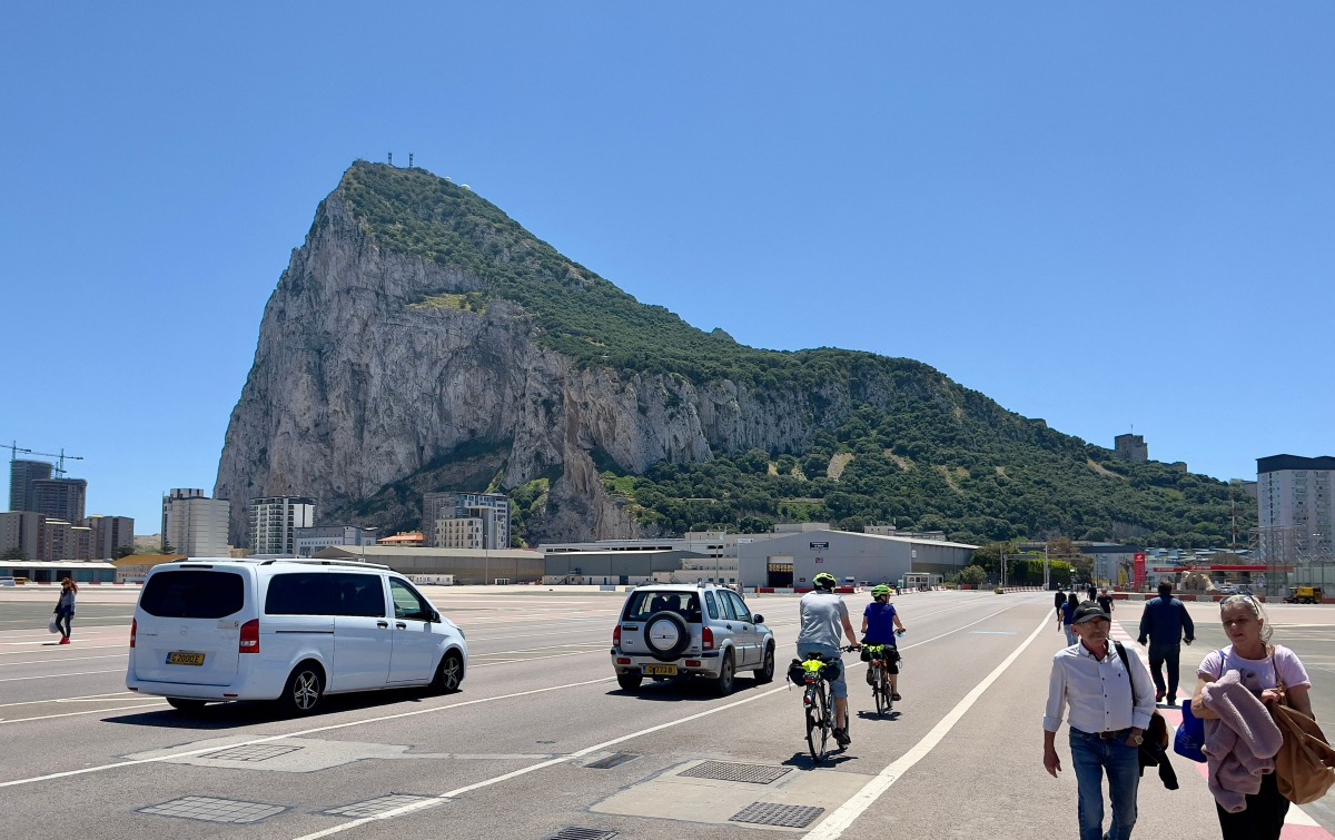 The Rock of Gibraltar is seen in the background as people and cars cross over the Gibraltar airport runway after crossing the border between Spain and the British territory of Gibraltar on May 5, 2022. (Photo by Daniel SLIM / AFP)