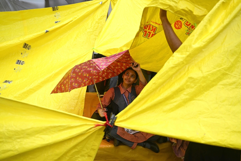 A school girl takes shelter under an umbrella at Jantar Mantar in New Delhi on July 24, 2026. (Photo by Arun Sankar / AFP)
 
