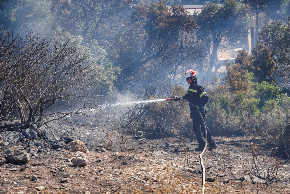 A firefighter uses a waterhose as he works to battle a wildfire, south of Rethymno in the Greek island of Crete on July 30, 2026.(Photo by Costas METAXAKIS / AFP)