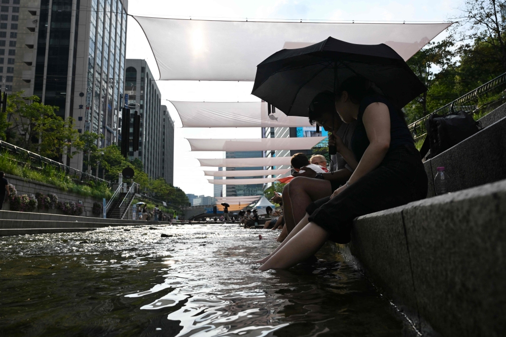 People cool off below sunshades over the Cheonggyecheon Stream in Seoul on August 3, 2026. (Photo by Greg Baker / AFP)