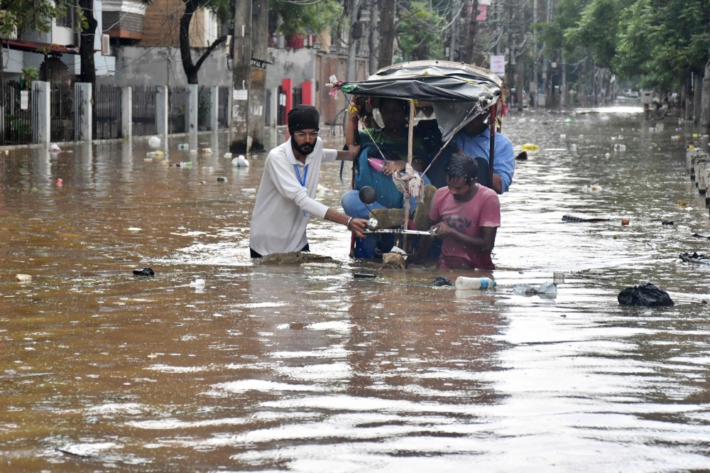 Residents wade through a flooded street following heavy monsoon rains in Guwahati on August 4, 2026. (Photo by Biju BORO / AFP)