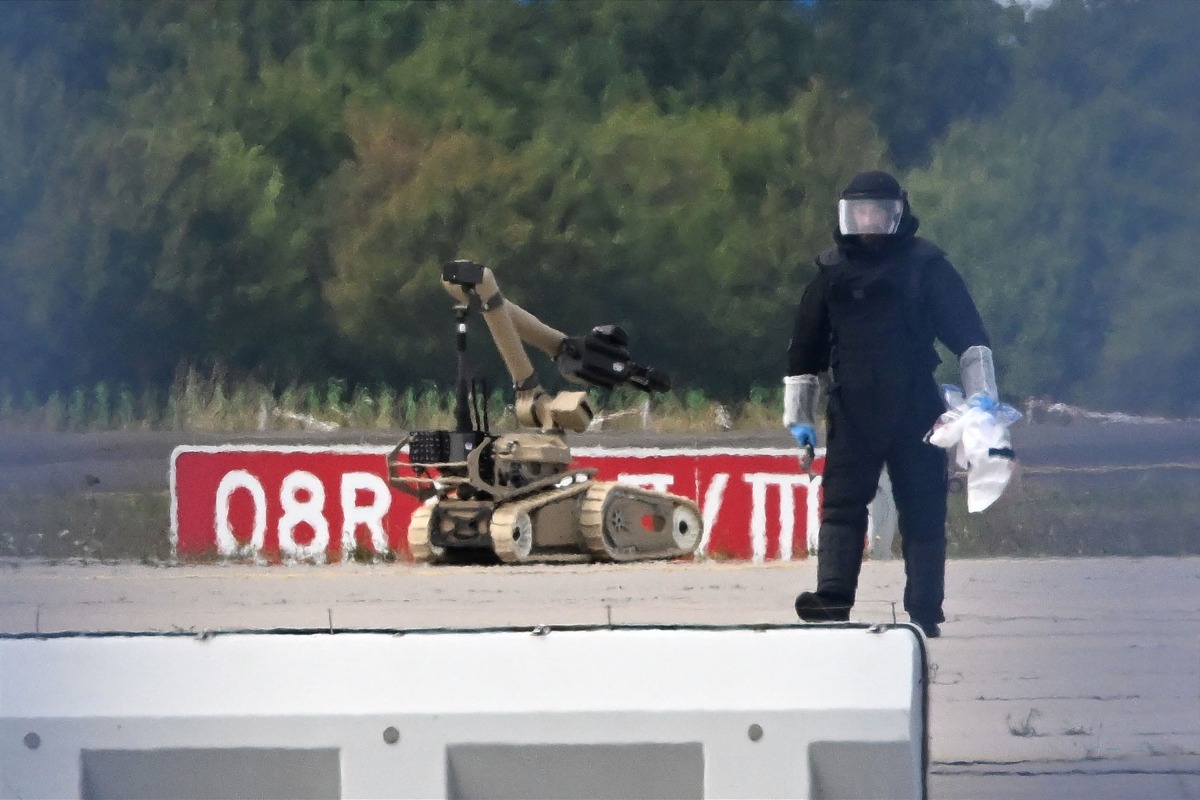 A forensic technician is at work alongside a bomb disposal robot near a Ukrainian cargo plane at Leipzig/Halle Airport in Schkeuditz, eastern Germany on August 5, 2026, after an explosives-laden drone was found near the plane overnight, and another aircraft collided with an unknown flying object mid-air nearby before landing safely. Photo by Hendrik Schmidt / dpa / AFP