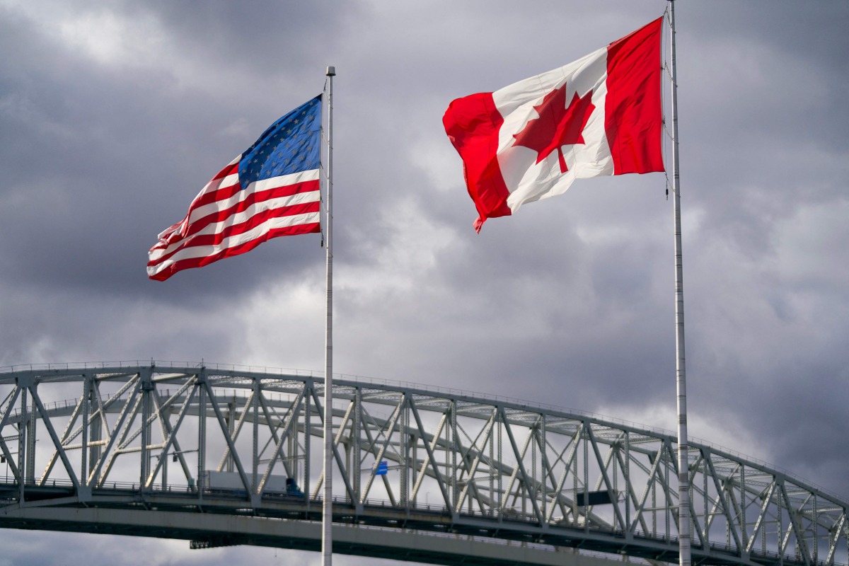 The US and Canadian flags flutter next to the Blue Water Bridge border crossing in Point Edward, Ontario, on October 24, 2025. (Photo by Geoff Robins / AFP)