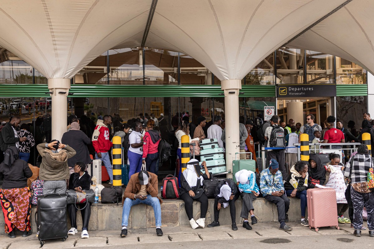 Stranded passengers sit on the pavement as they wait with their luggage by the departure terminal of the Jomo Kenyatta International Airport (JKIA) after staff from the Kenya Airports Authority (KAA) and Kenya Civil Aviation Authority (KCAA) airport workers' go-slow strike action continued into its second day, in Nairobi, on August 31, 2026. Photo by SIMON MAINA / AFP