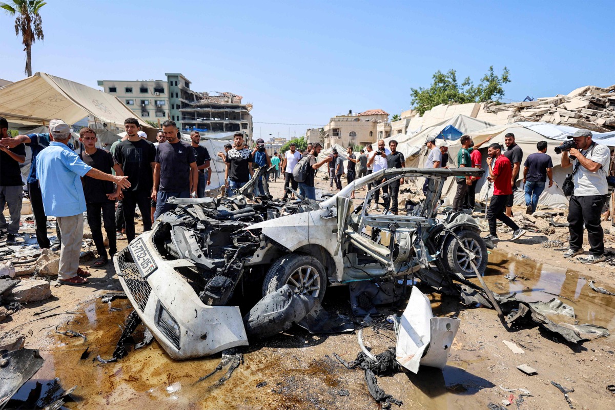 People gather around a destroyed vehicle following an Israeli strike in the Rimal neighbourhood of Gaza City on September 1, 2026. (Photo by Omar AL-QATTAA / AFP)