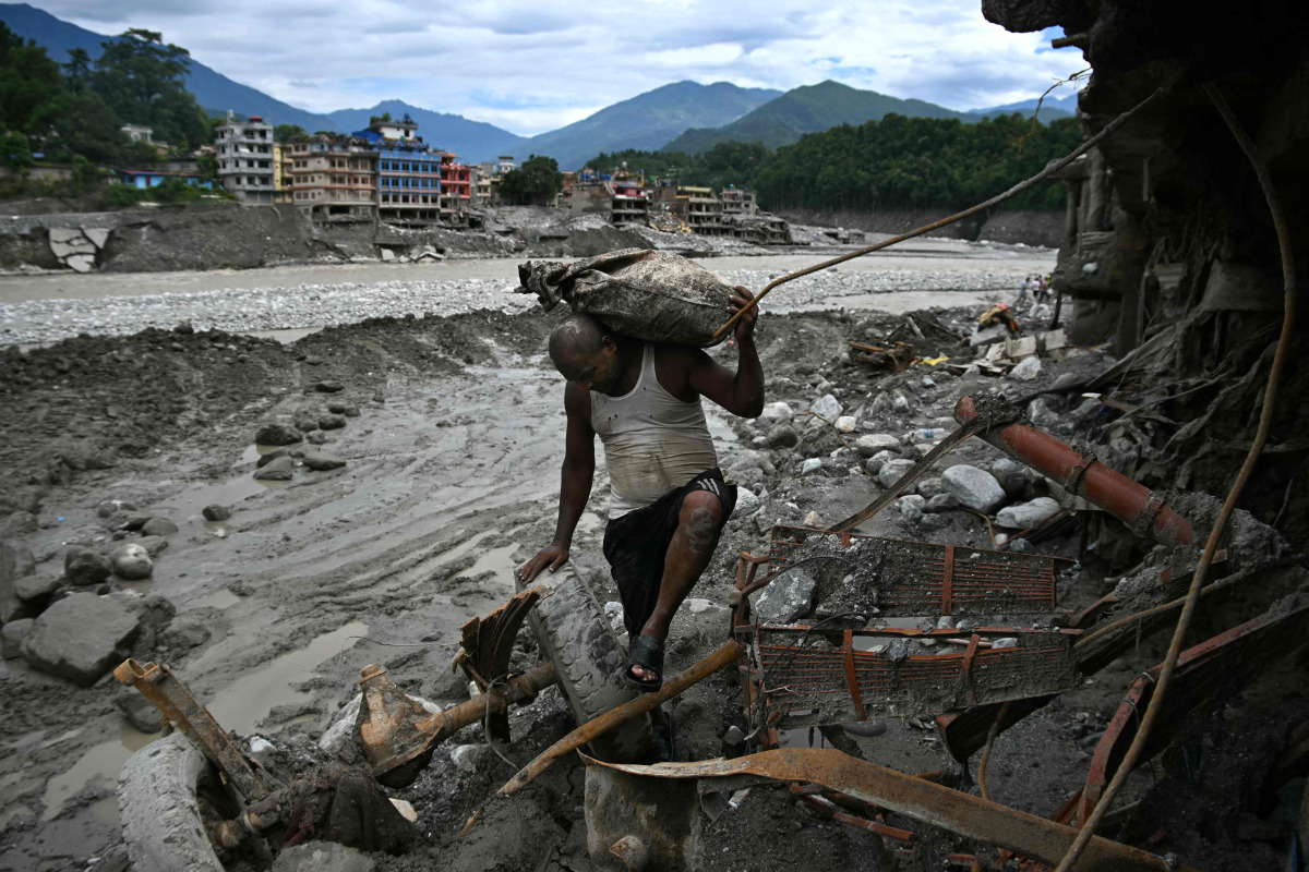 A man carrying his belongings walks past a damaged house in the aftermath of flash floods at Trishuli in Nepal's Nuwakot district on September 11, 2026. (Photo by Prakash MATHEMA / AFP)