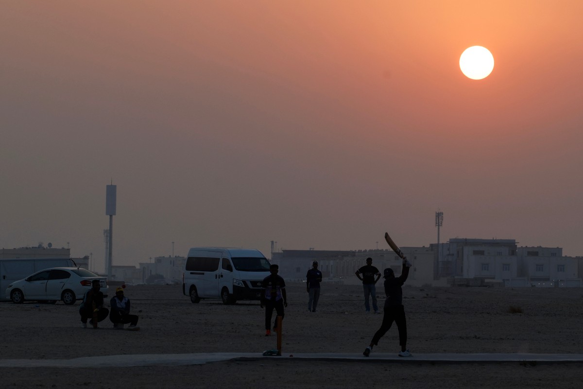 Foreign workers play cricket at sunset in Doha on October 1, 2026. (Photo by KARIM JAAFAR / AFP)
