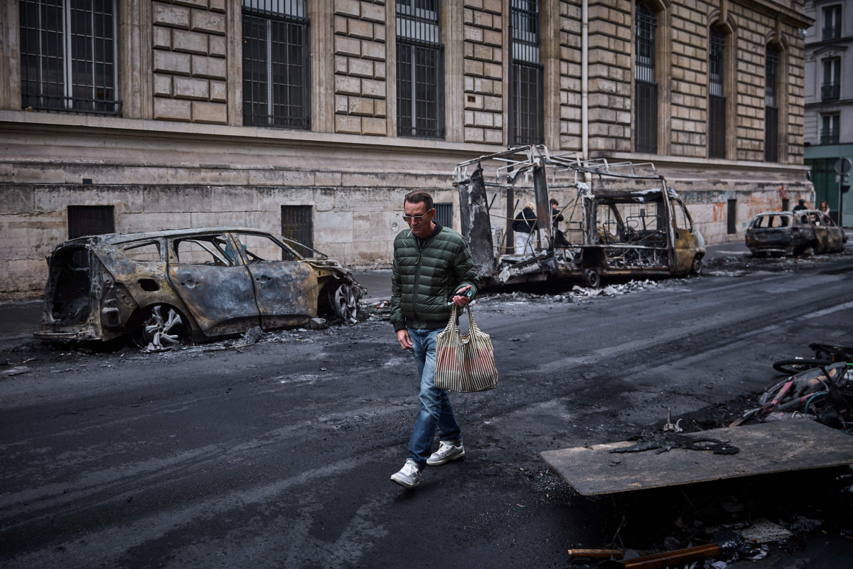 A man walks past a row of burnt out vehicles on Rue Yves Toudic destroyed after a nationwide protest against the 